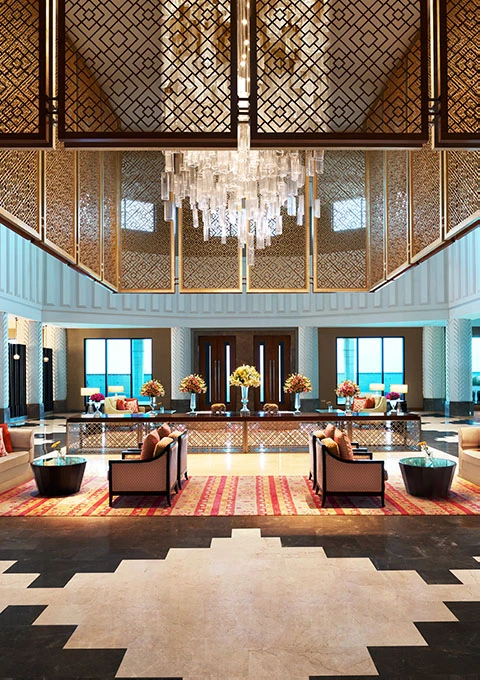 The grand lobby of The Leela Gandhinagar with a gilded jaali screen and crystal chandelier