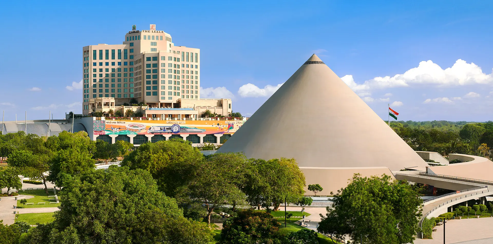 Panoramic view of The Leela Gandhinagar tower beside the landmark Dandi Kutir cone, framed by manicured gardens